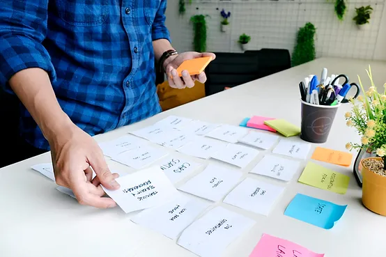 A person in a blue plaid shirt working at a desk, surrounded by sticky notes and other office supplies.